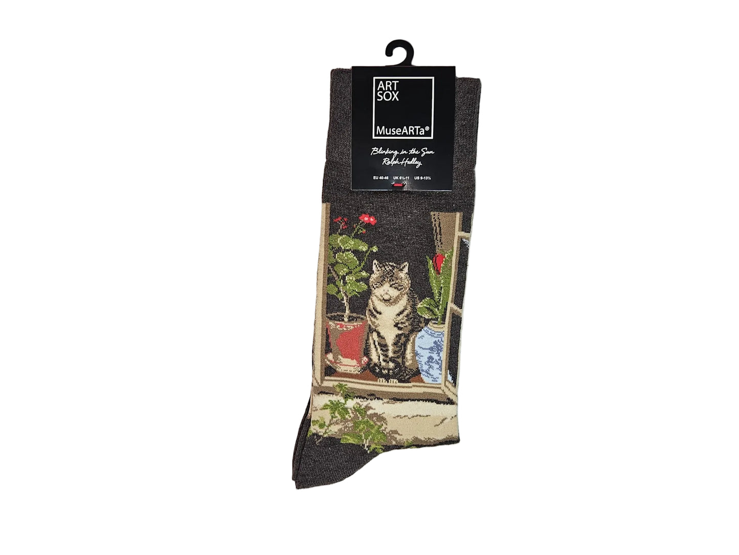 Dark gray socks with a printed illustration of a cat sitting by a window next to potted plants, hanging from a black card by MuseArt on a light gray background.