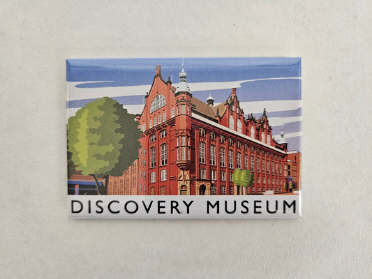 A rectangular printed magnet featuring an illustration of the Discovery Museum building, with the words 'DISCOVERY MUSEUM' printed along the bottom, shown against a light textured background.