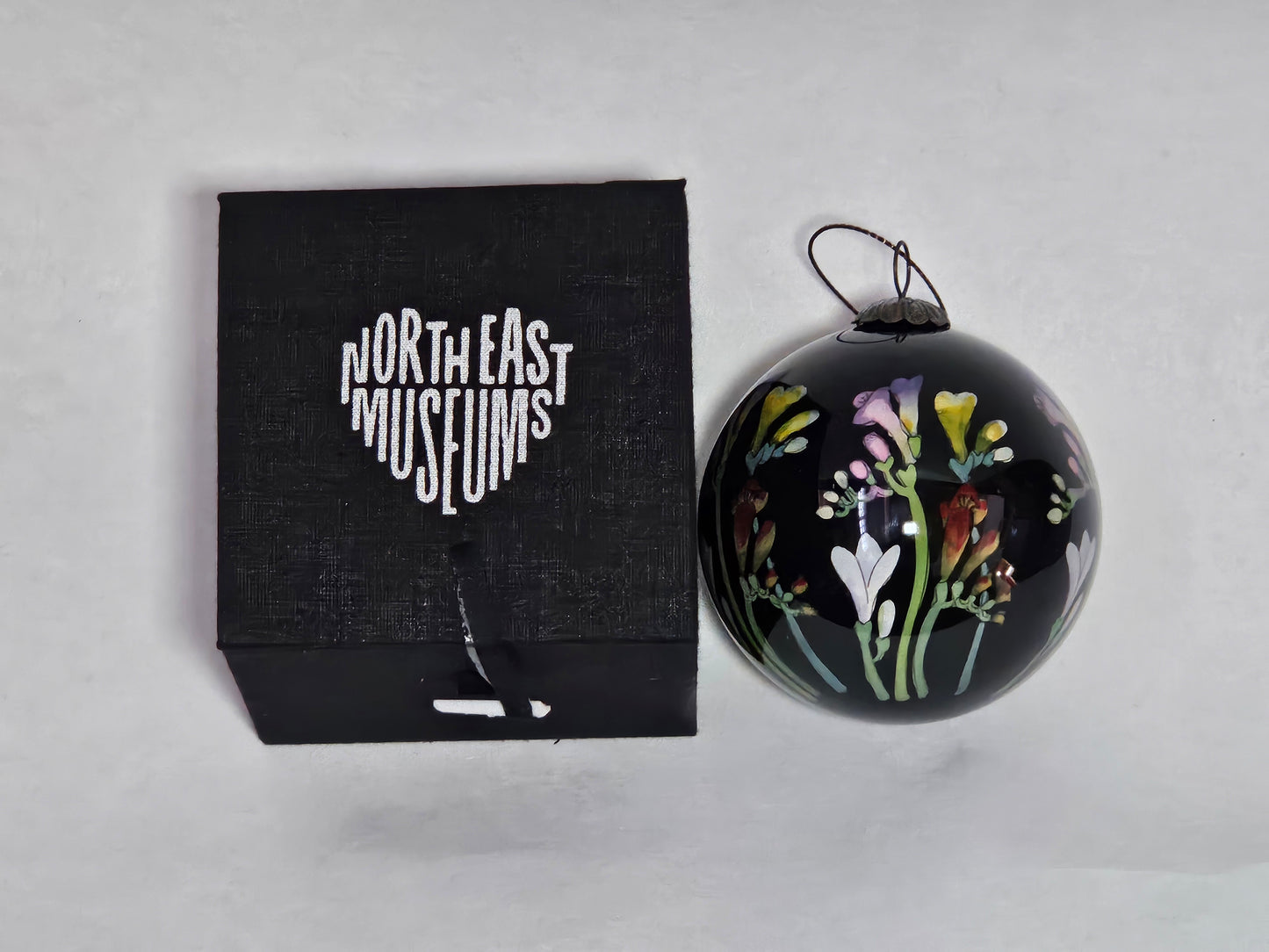 Black ornament with floral design next to a black box labeled 'North East Museums' on a light gray background