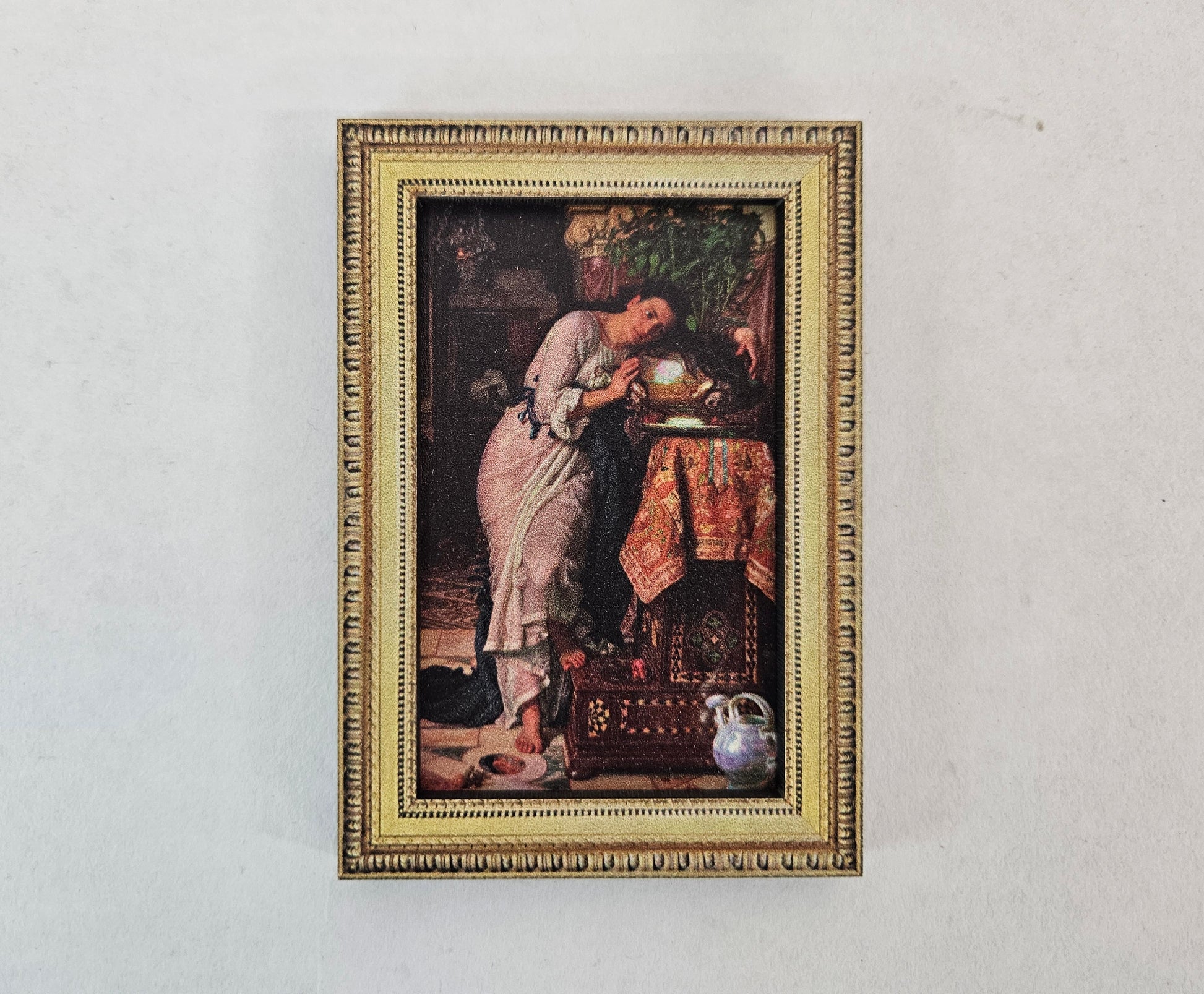 A gold framed painting depicting a dark haired woman in a light coloured dress leaning over a table holding a gold bowl containing a basil plant. 